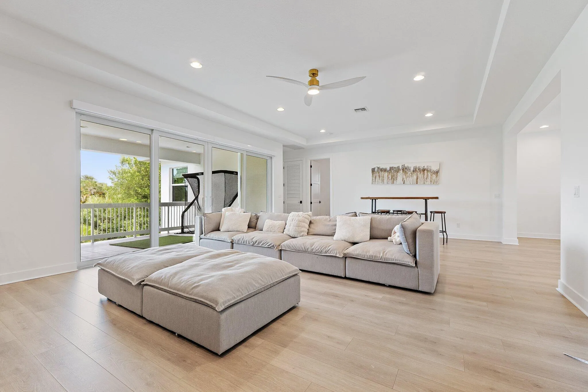 Living room with sofa, ottoman, high ceiling, and sliding doors to balcony