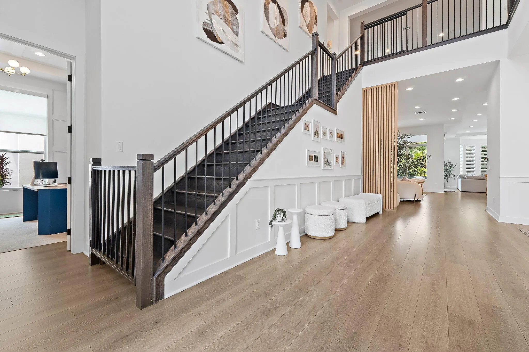Foyer with staircase, black iron railing, gallery wall, and wood flooring