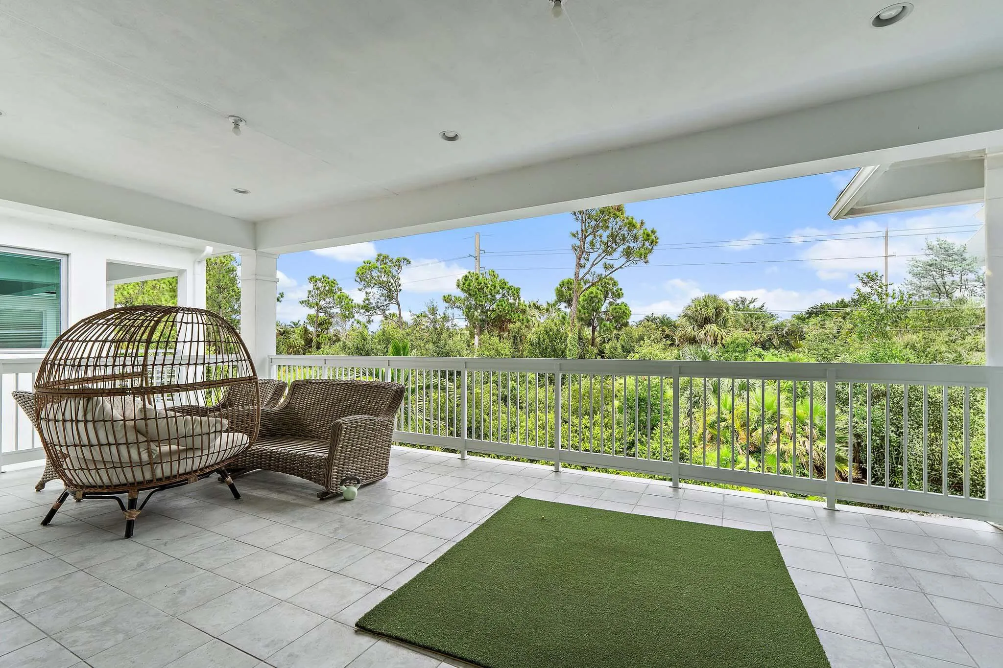 Covered balcony with wicker seating, rug, and tree-lined view