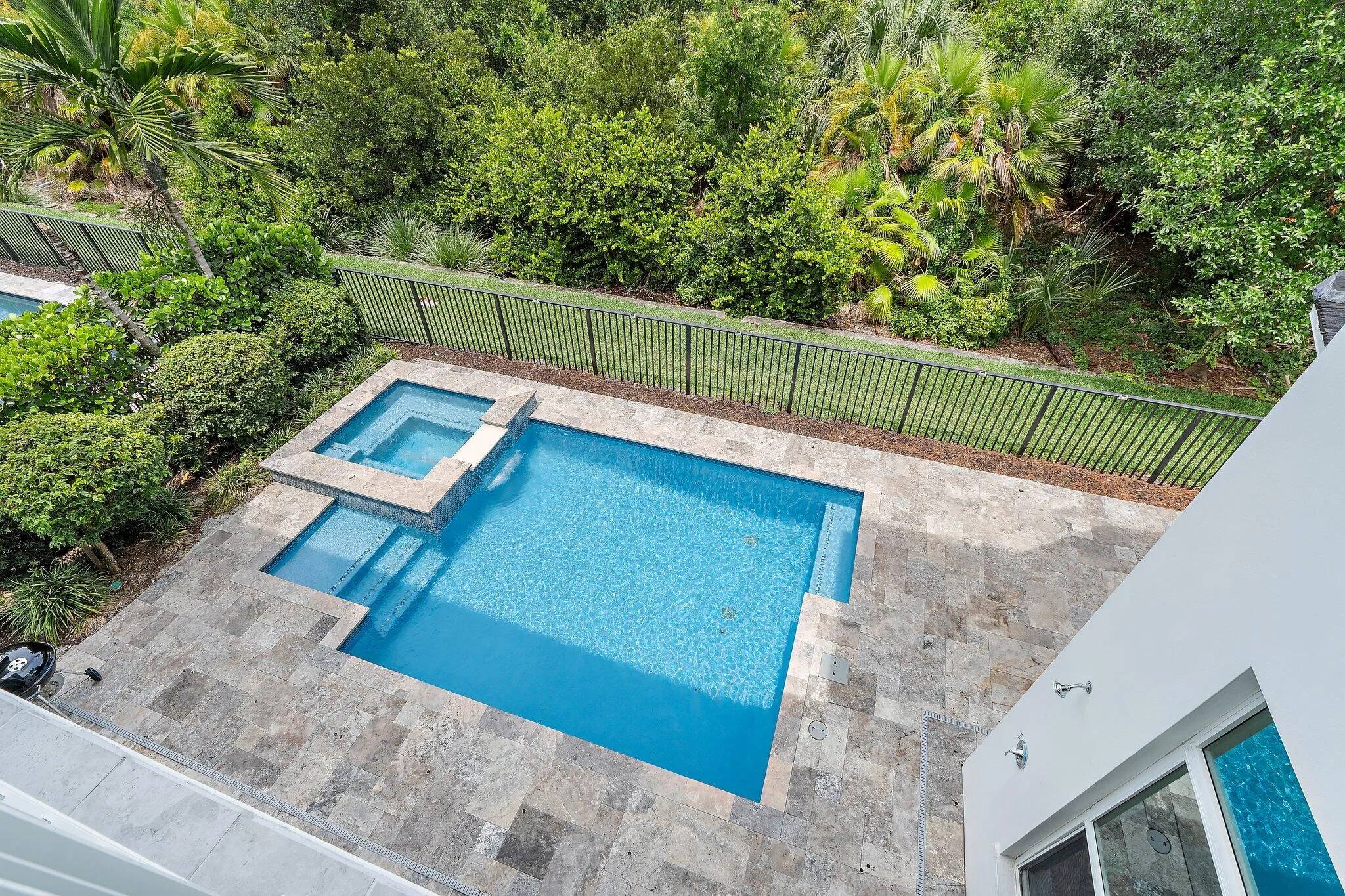 Aerial view of pool and spa with paver deck and fenced tropical landscaping