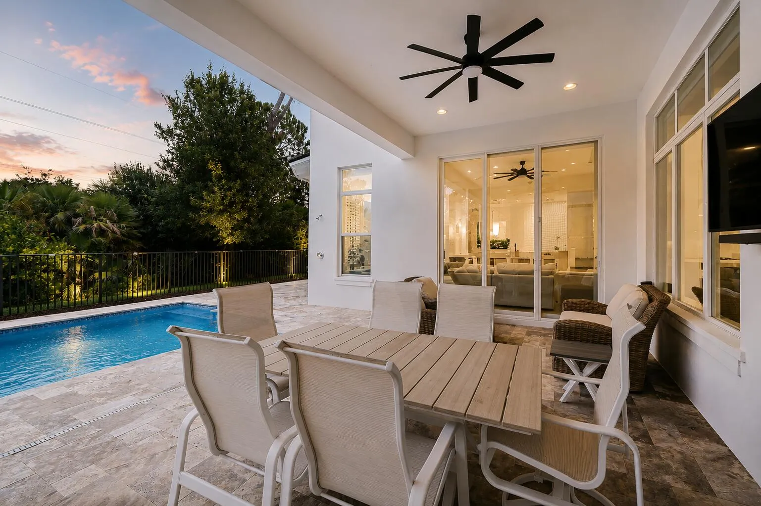 Covered outdoor patio with dining table, chairs, ceiling fans, and pool view