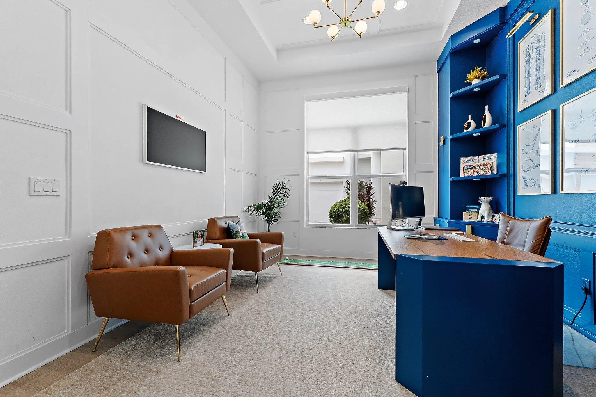 Home office with navy blue built-in desk and shelving, leather armchairs, and wall-mounted TV
