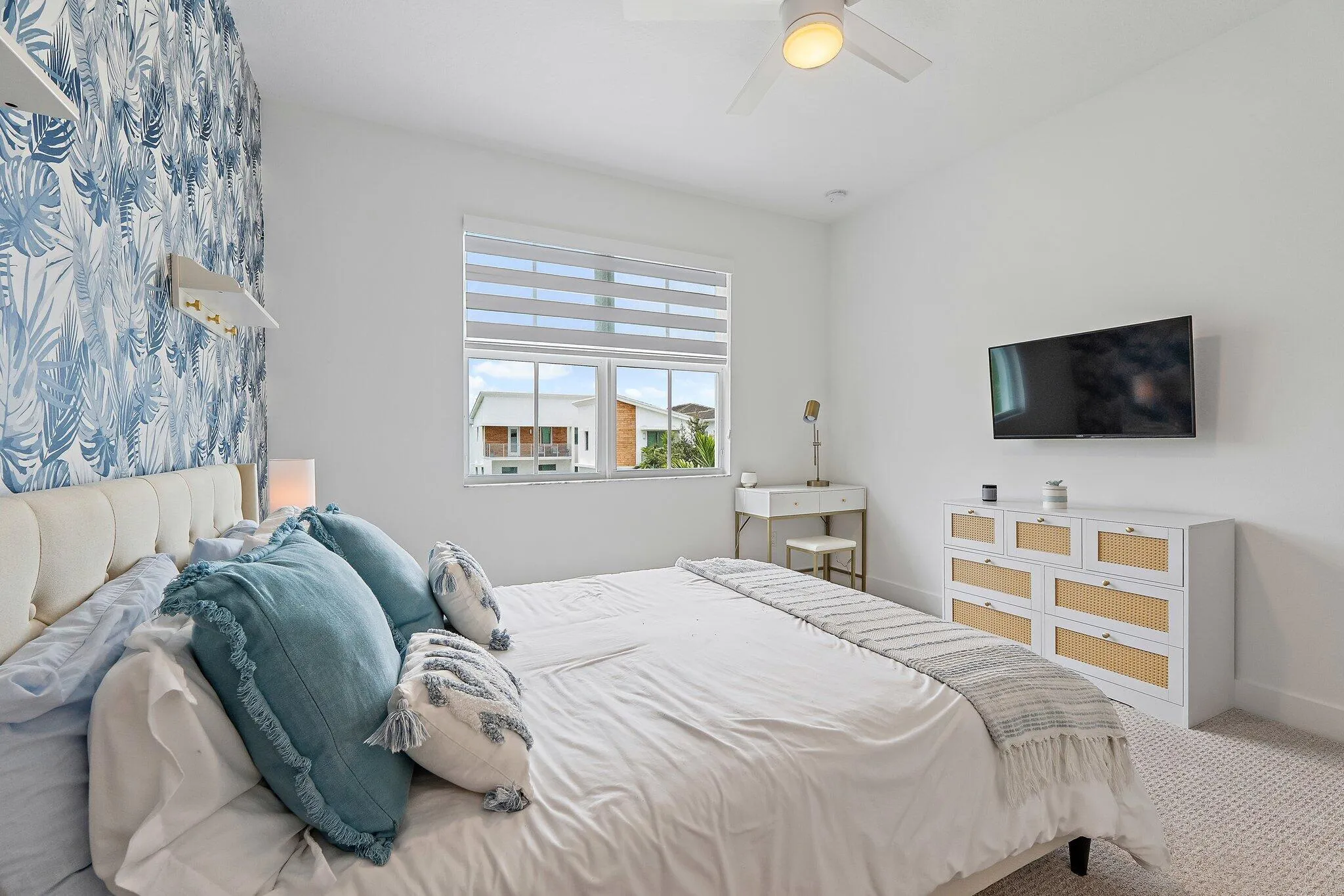 Bedroom with blue floral accent wallpaper, mounted TV, and dresser