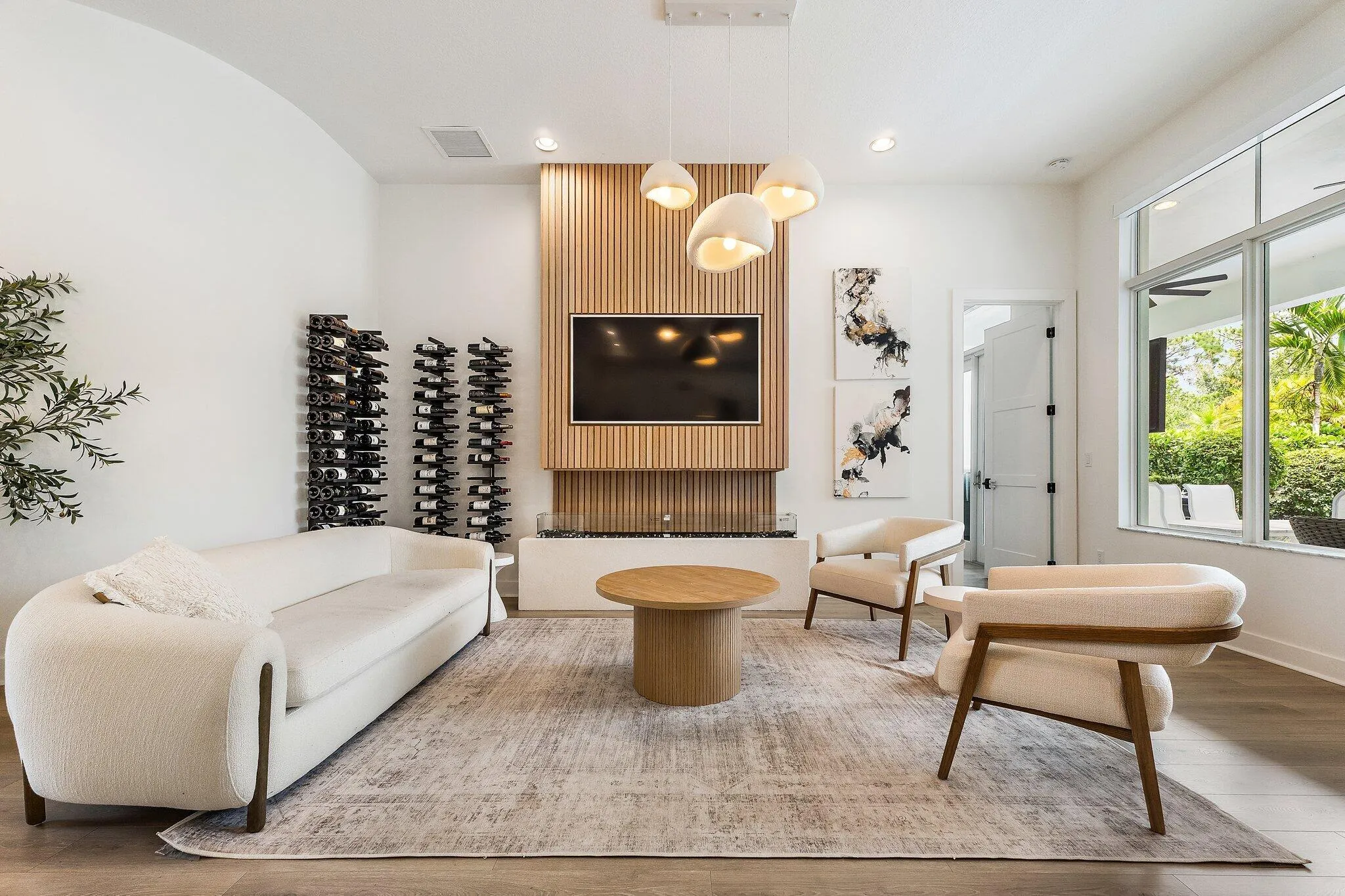 Living room with wood accent wall, wine storage shelving, mounted TV, and round coffee table