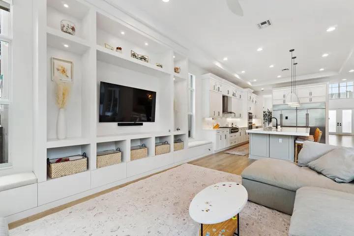 Living area with built-in shelving, mounted TV, and open view to kitchen
