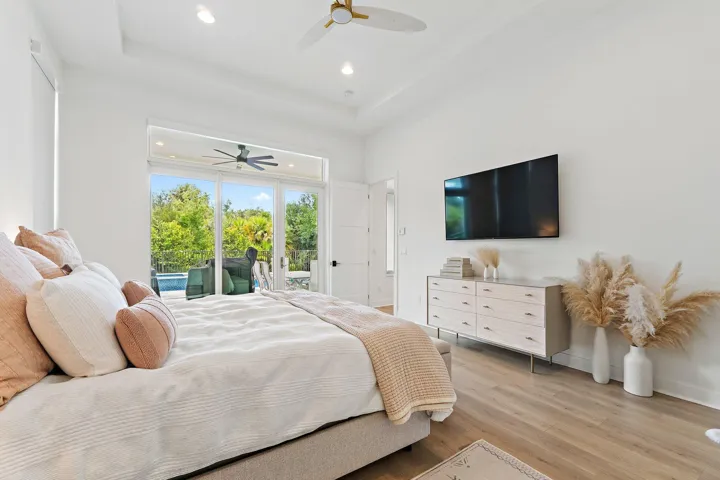 Bedroom with bed, nightstands, wall-mounted TV, ceiling fan, and sliding glass doors