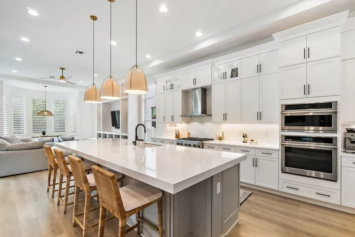 Kitchen with white cabinetry, large island, wood bar stools, and double wall ovens