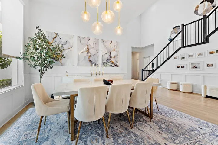 Dining area with round table, upholstered chairs, chandelier, and area rug near staircase