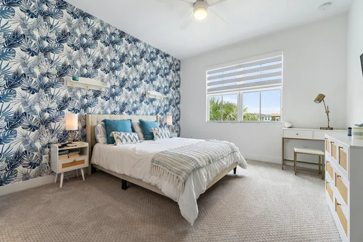 Bedroom with blue floral wallpaper, upholstered bed, and desk