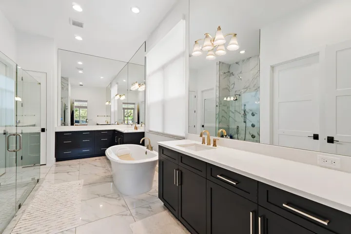 Primary bathroom with dual vanity, dark cabinetry, freestanding soaking tub, and glass shower