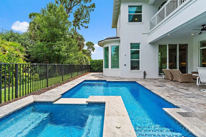 Rear exterior with pool, patio seating, and black fencing