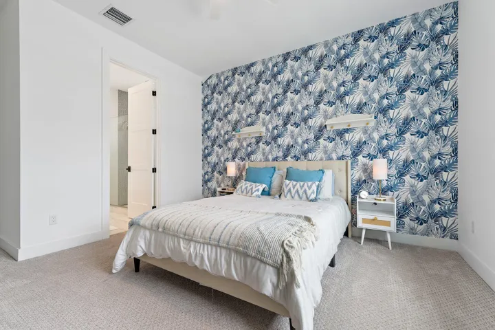 Bedroom with blue floral accent wall, white nightstands, and carpet flooring