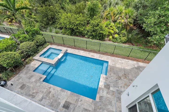 Aerial view of pool and spa with paver deck and fenced tropical landscaping
