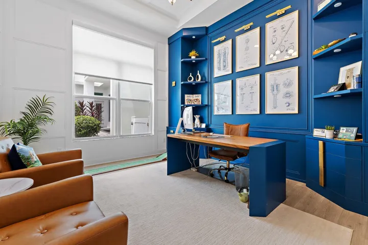 Home office with navy blue built-in desk and shelving, gallery wall, and leather armchairs