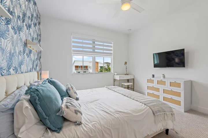 Bedroom with blue floral accent wallpaper, mounted TV, and dresser