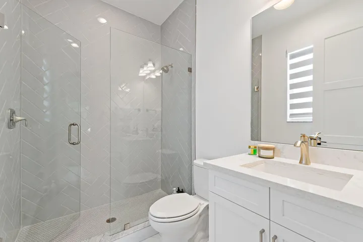 Bathroom with glass shower, white vanity, and marble tile