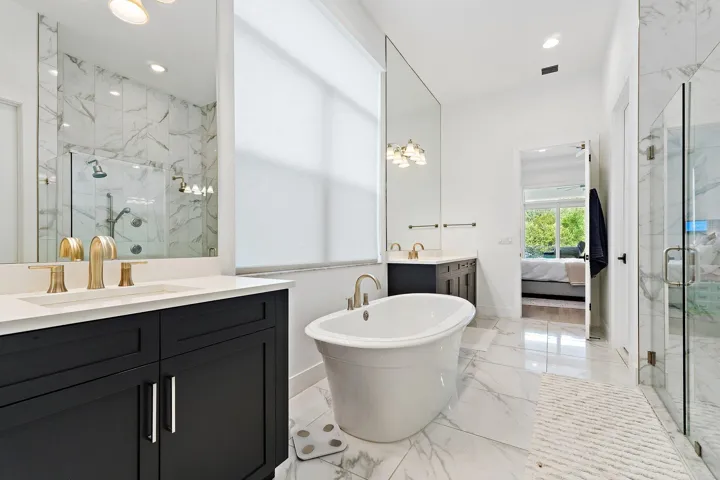 Bathroom with dark cabinetry, dual vanity, freestanding tub, and marble tile