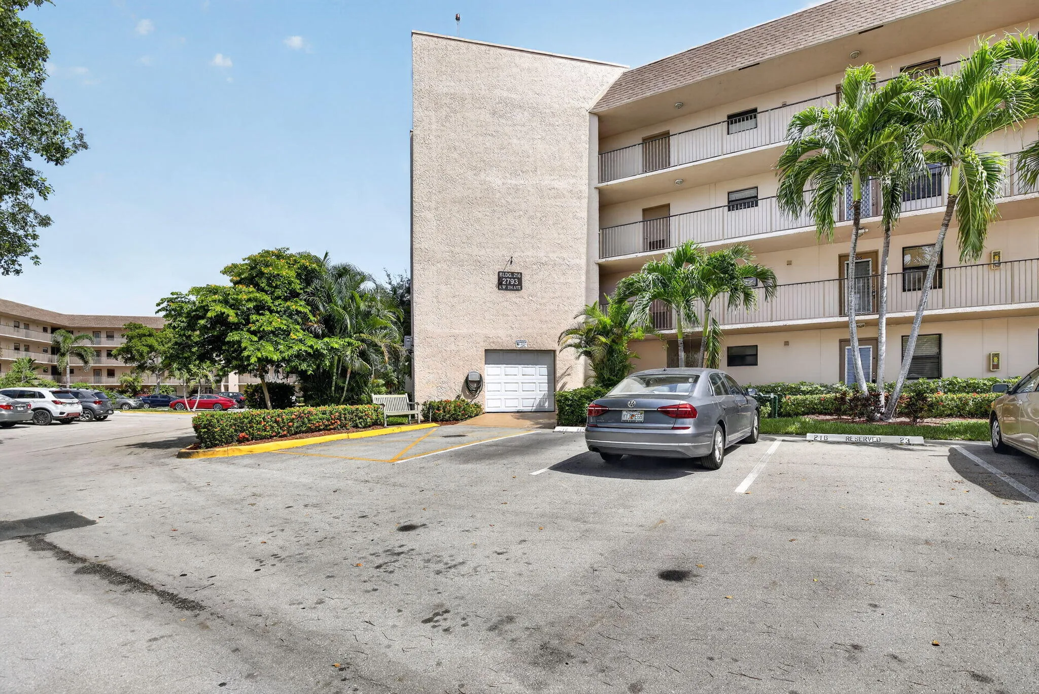 Multi-story building featuring balconies with metal railings, a stucco exterior, and multiple palm trees