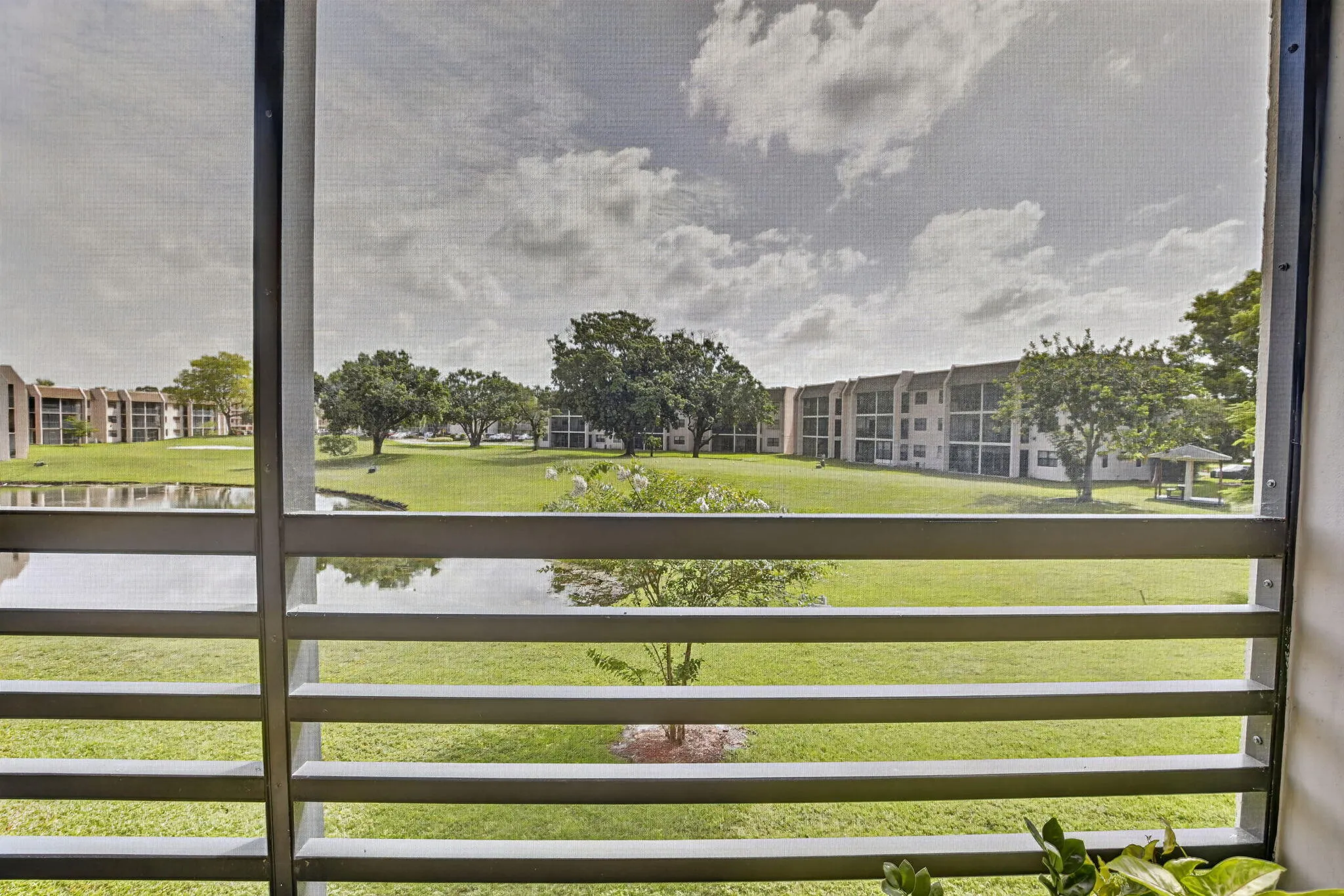 Screened balcony overlooking expansive green space with mature trees and a tranquil lake