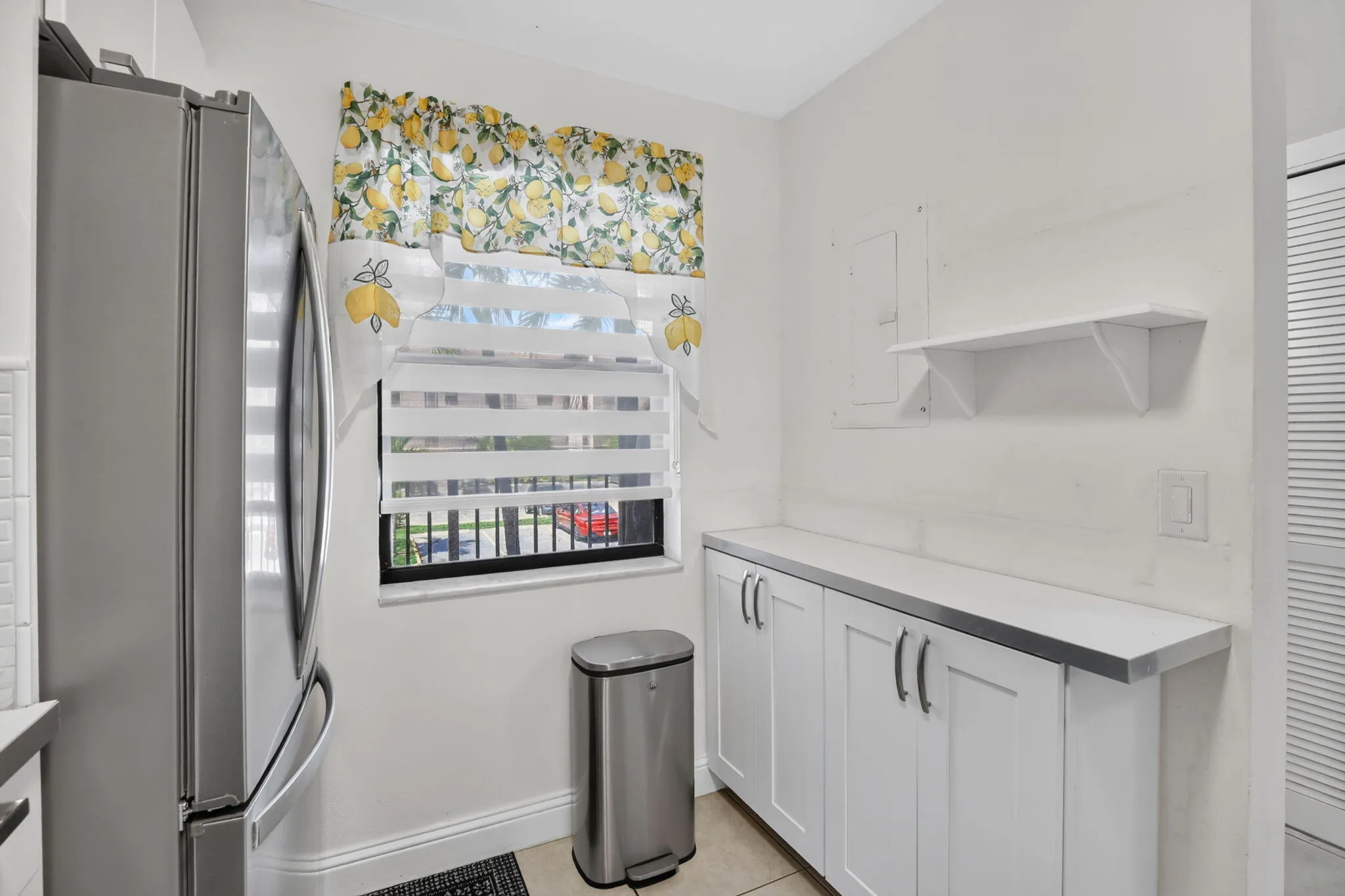 Kitchen area featuring white cabinetry with silver hardware, a light-colored countertop, and a window with horizontal blinds