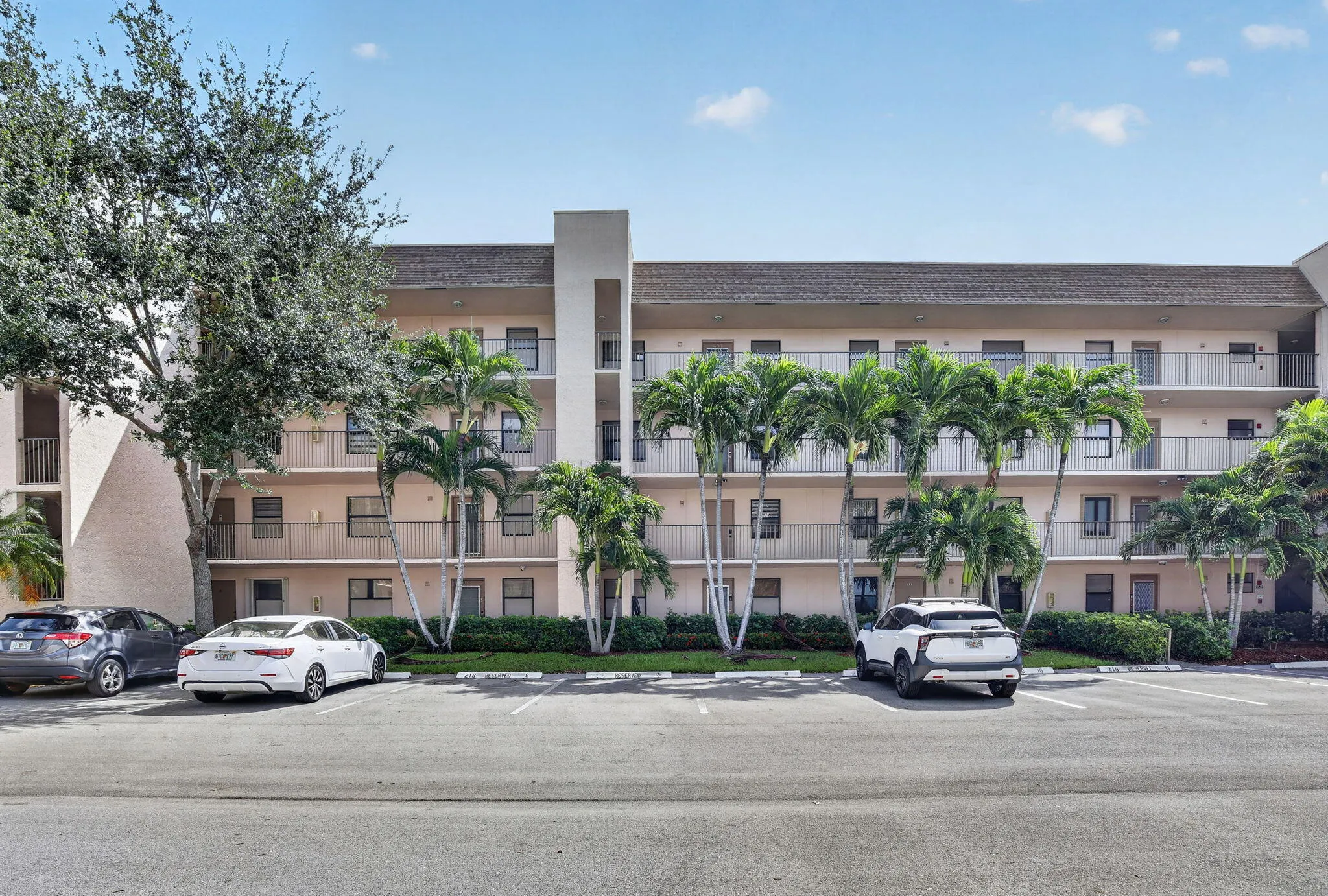 Multi-story building featuring stucco exterior, multiple balconies with metal railings, and an asphalt parking area with assigned and guest parking