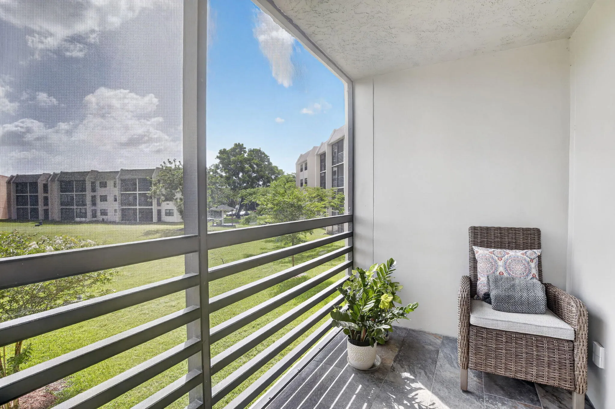Screened balcony featuring tiled floor, white painted walls, and metal railings overlooking green spaces and distant buildings