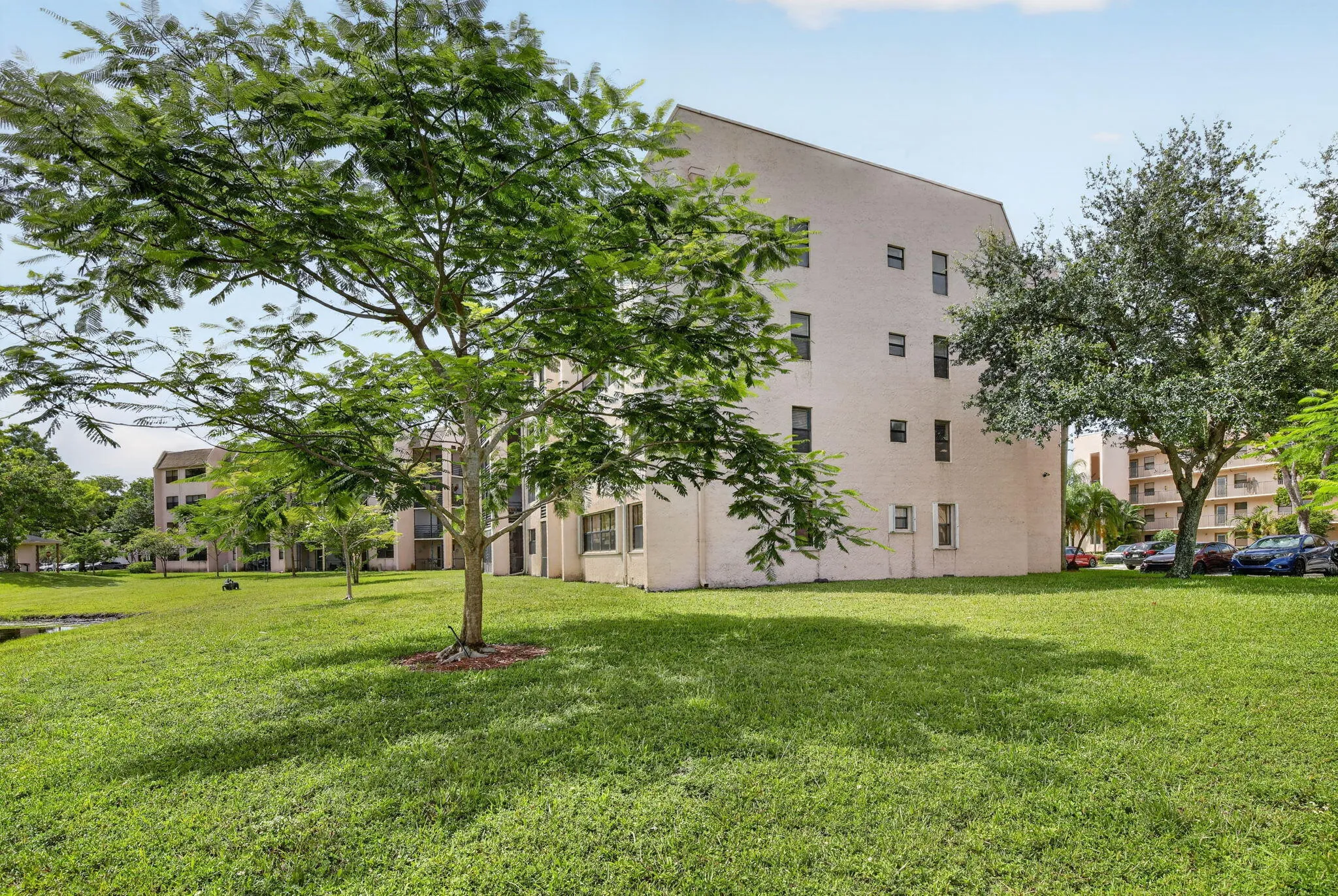 Expansive green space featuring mature trees and a tranquil pond, complementing the multi-story exterior with multiple windows