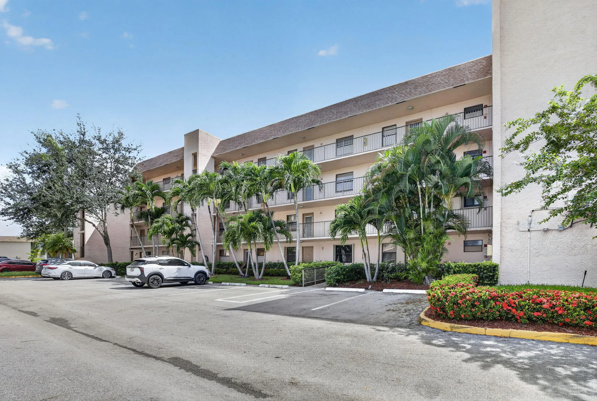 Multi-story building exterior with balconies, lush palm trees, and mature landscaping