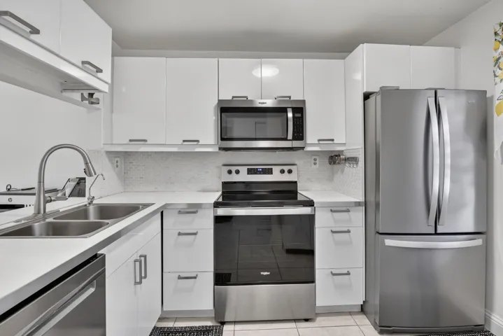 Contemporary kitchen featuring white cabinetry with brushed nickel hardware, newer stainless steel appliances, a double stainless-steel sink with a pull-down faucet, white countertops, and a mosaic tile backsplash
