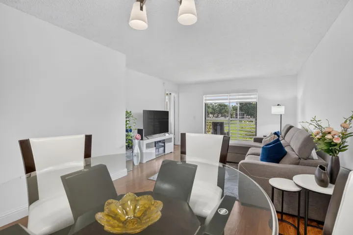 Bright open-concept living area with laminate flooring, white walls, and a large window overlooking lake and green space