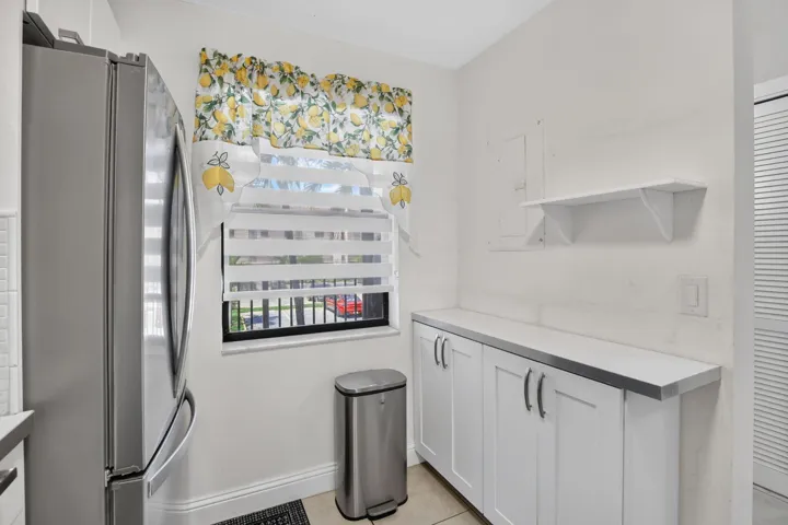 Kitchen area featuring white cabinetry with silver hardware, a light-colored countertop, and a window with horizontal blinds