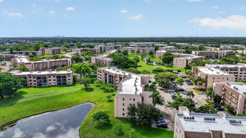 Aerial perspective showcasing multiple residential buildings, lush green spaces, a reflective lake, and paved parking areas