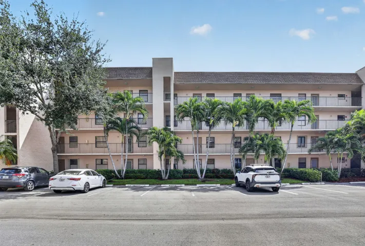Multi-story building featuring stucco exterior, multiple balconies with metal railings, and an asphalt parking area with assigned and guest parking