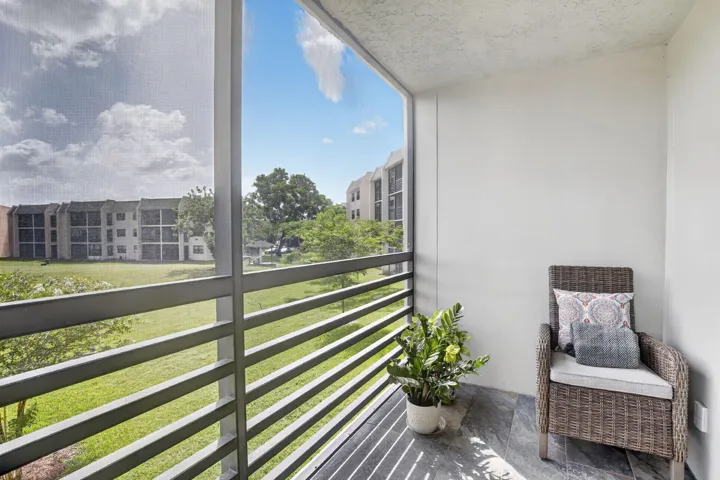 Screened balcony featuring tiled floor, white painted walls, and metal railings overlooking green spaces and distant buildings