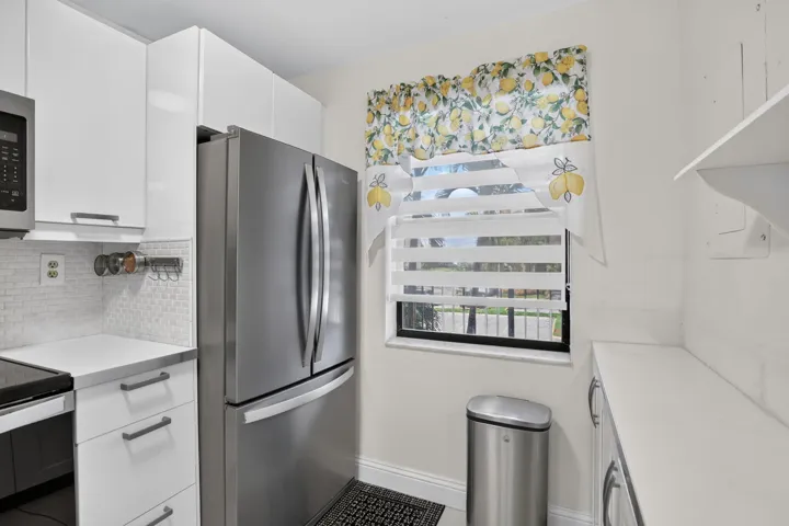 Contemporary kitchen featuring white cabinetry, stainless steel appliances, a white mosaic tile backsplash, and a built-in window with horizontal blinds