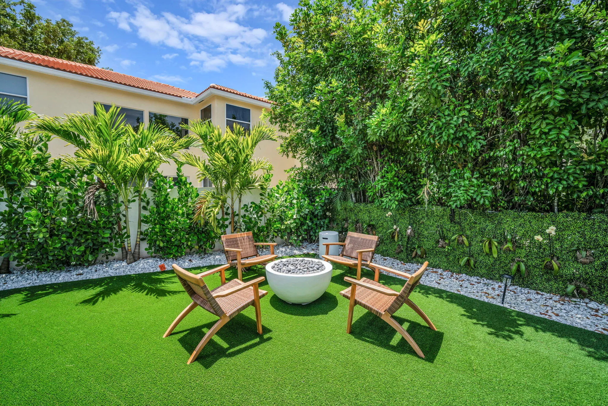Manicured outdoor area featuring artificial turf, a central fire pit, and white pebble borders