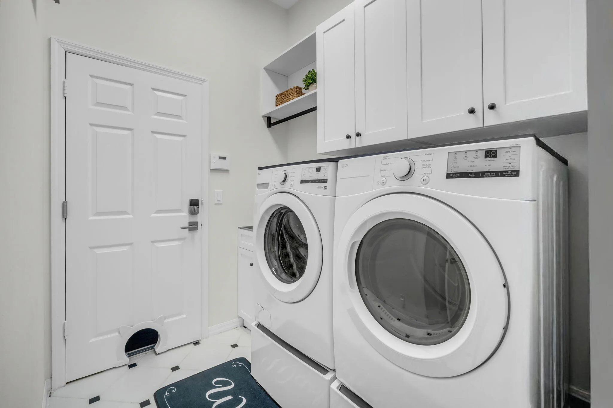 Dedicated laundry area featuring white cabinetry, a built-in shelf, and black and white floor tiling