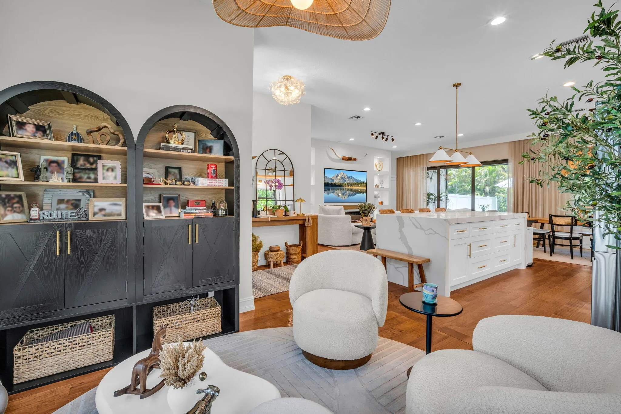 Open-concept living space featuring wood-finish flooring, a contemporary kitchen island with a waterfall countertop, and an arched built-in shelving unit