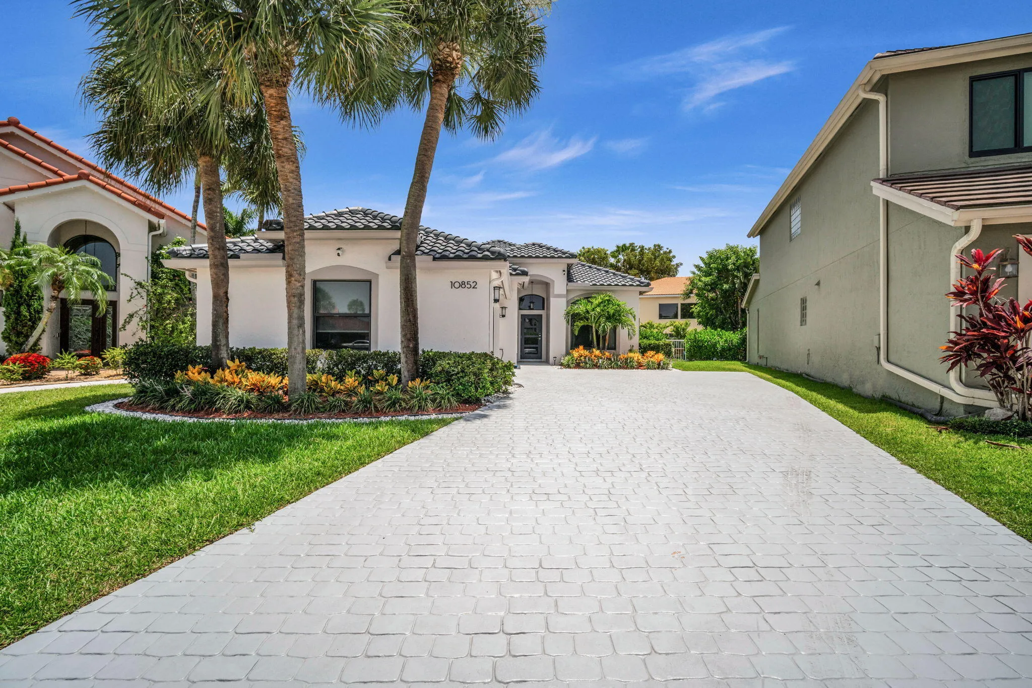 Exterior showcasing a paver driveway, mature palm trees, sculpted landscaping, a tiled roof, and a prominent arched entryway