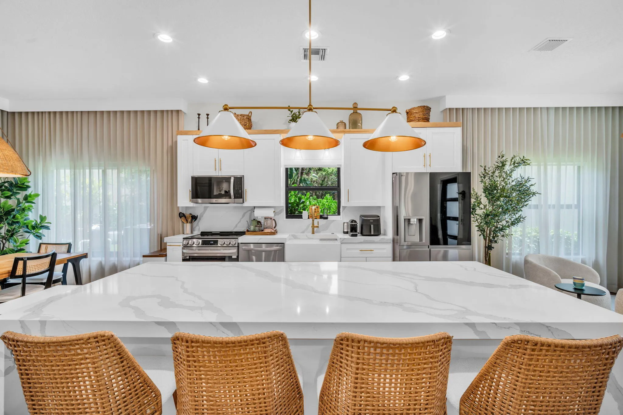 Expansive kitchen island with a white veined countertop, featuring white cabinetry, stainless steel appliances, and brass-finish pendant lighting