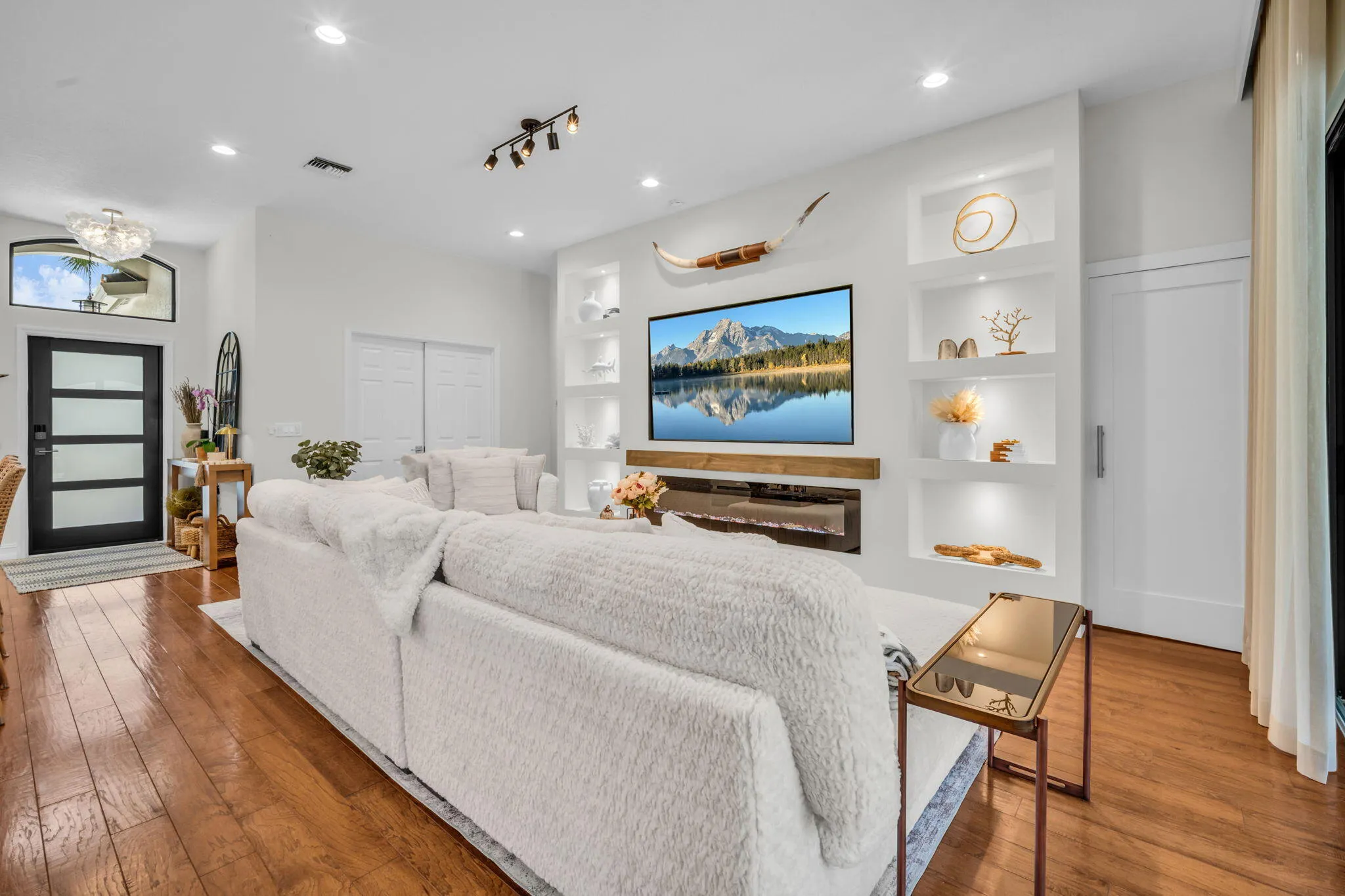 Bright living space featuring warm wood-finish flooring, recessed lighting, and a modern built-in entertainment wall with accent shelving