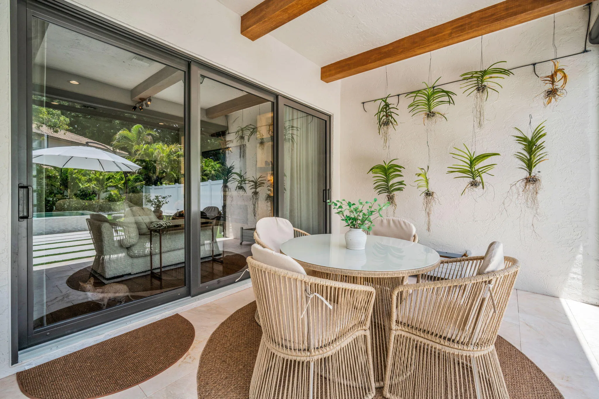 Covered patio featuring exposed wood beams, a textured white wall with suspended plants, and light-toned tile flooring