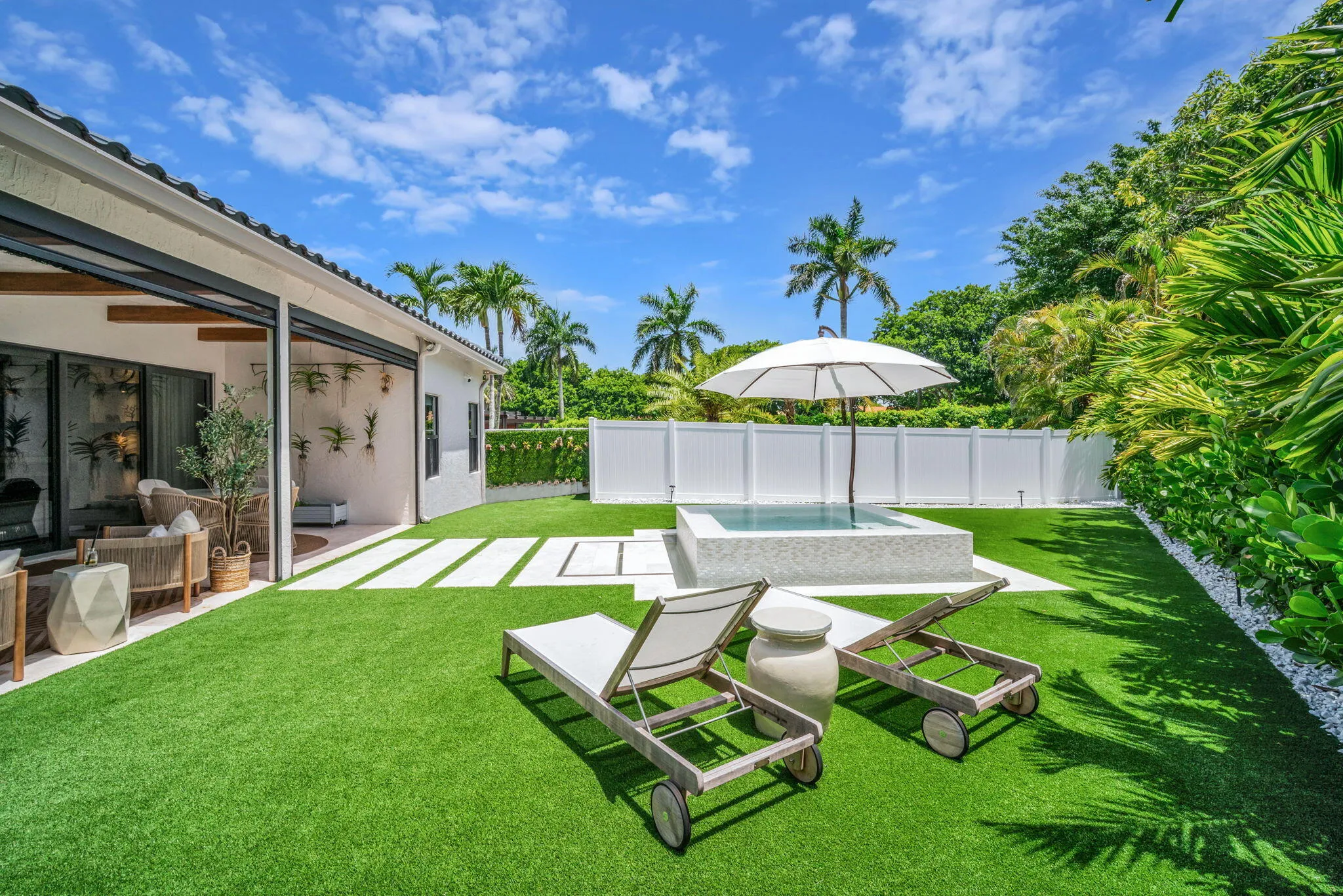 Expansive backyard featuring a central spa, artificial turf, and a white privacy fence