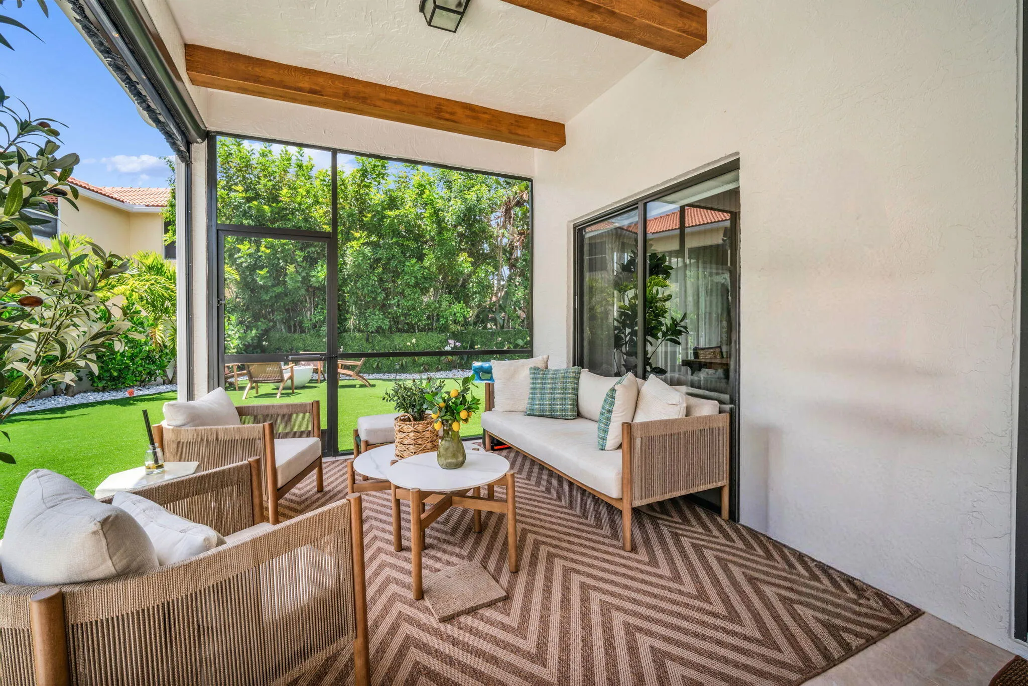 Screened outdoor patio featuring a textured area rug, exposed ceiling beams, and a sliding glass door