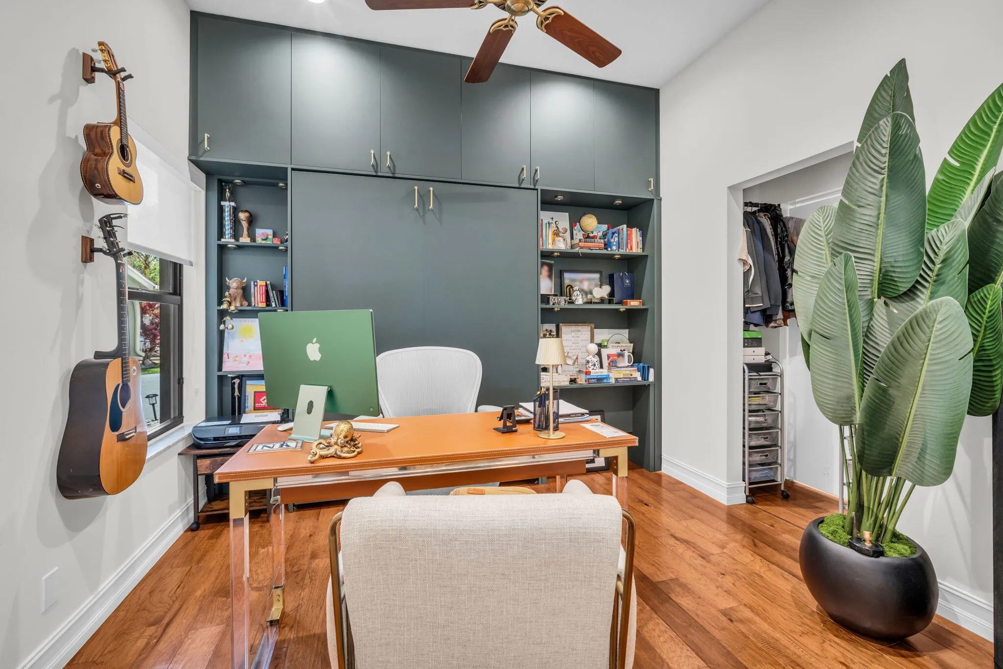 Dedicated room featuring extensive built-in cabinetry, integrated shelving, wood-finish flooring, a ceiling fan, and a functional window