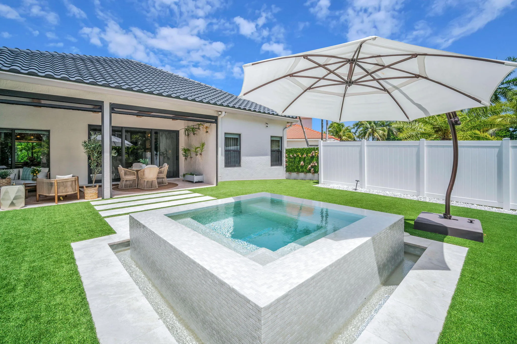 Backyard oasis featuring a square-shaped spa with tile surround, artificial turf, and a white privacy fence