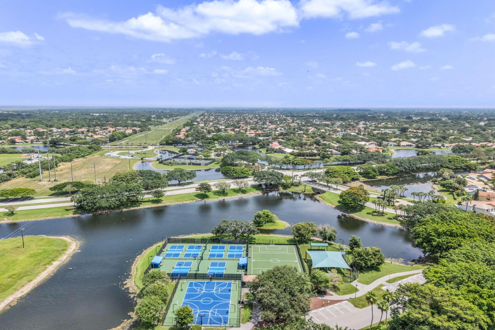 Expansive aerial showing multiple blue tennis courts, a blue basketball court, and a green soccer field