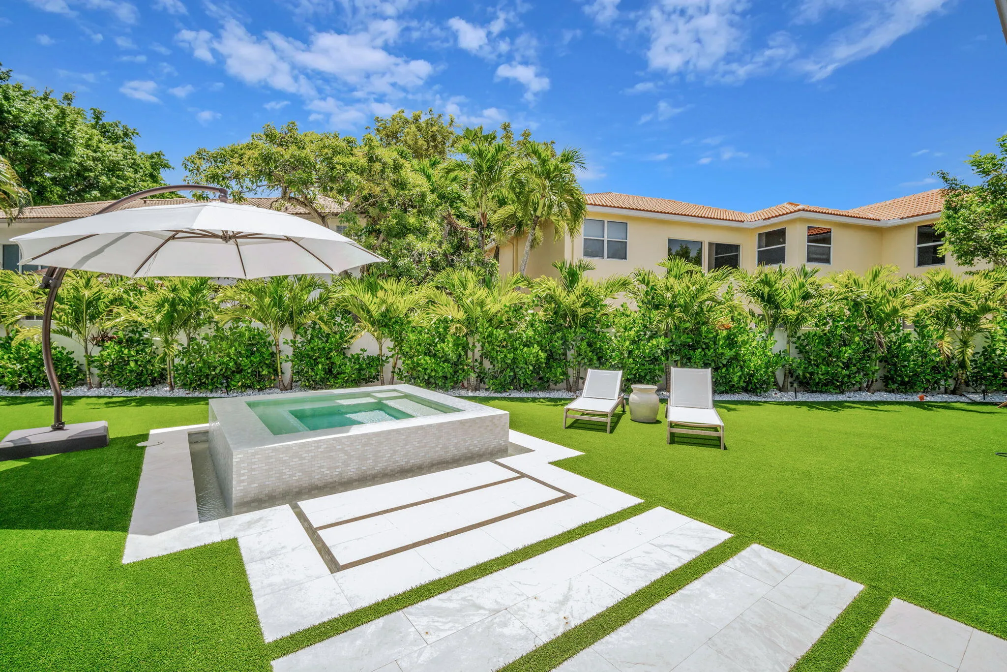Expansive backyard featuring a built-in spa with stone surround, artificial turf, and stepping stone pavers