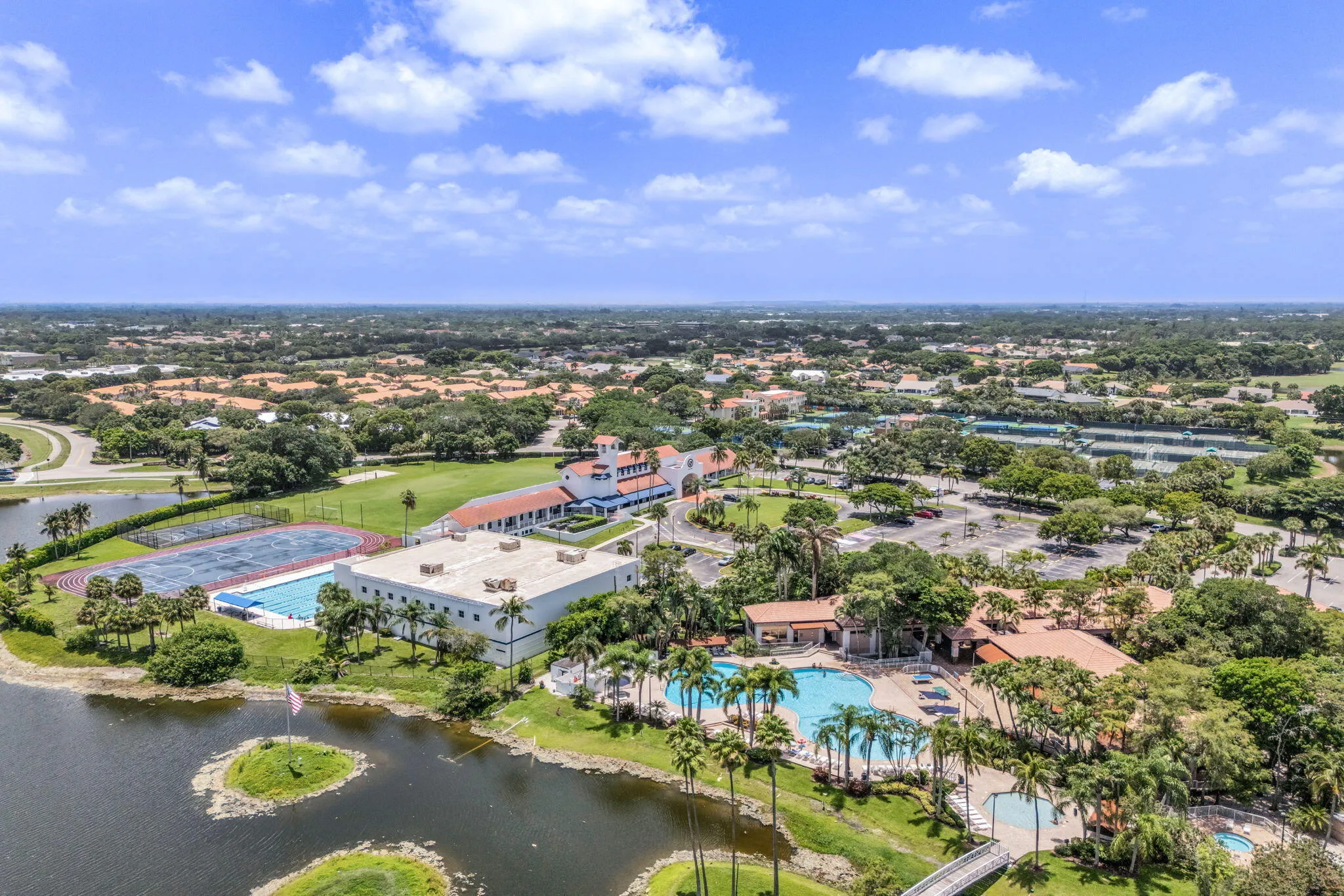 Aerial perspective showcasing expansive grounds with multiple buildings, a large swimming pool, tennis courts, and surrounding water features