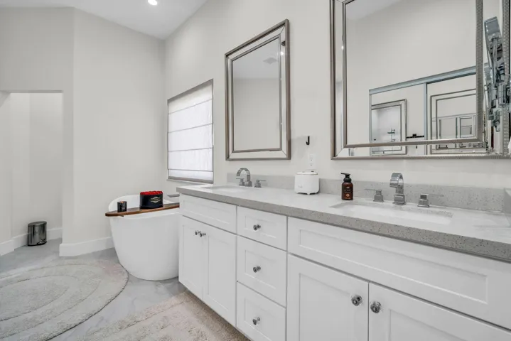 Bathroom featuring a freestanding soaking tub, dual vanities with integrated sinks, and individual framed mirrors